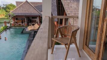 Une chaise en bois près d’une piscine, une porte vitrée et, au fond, un bâtiment avec un toit en tuiles.