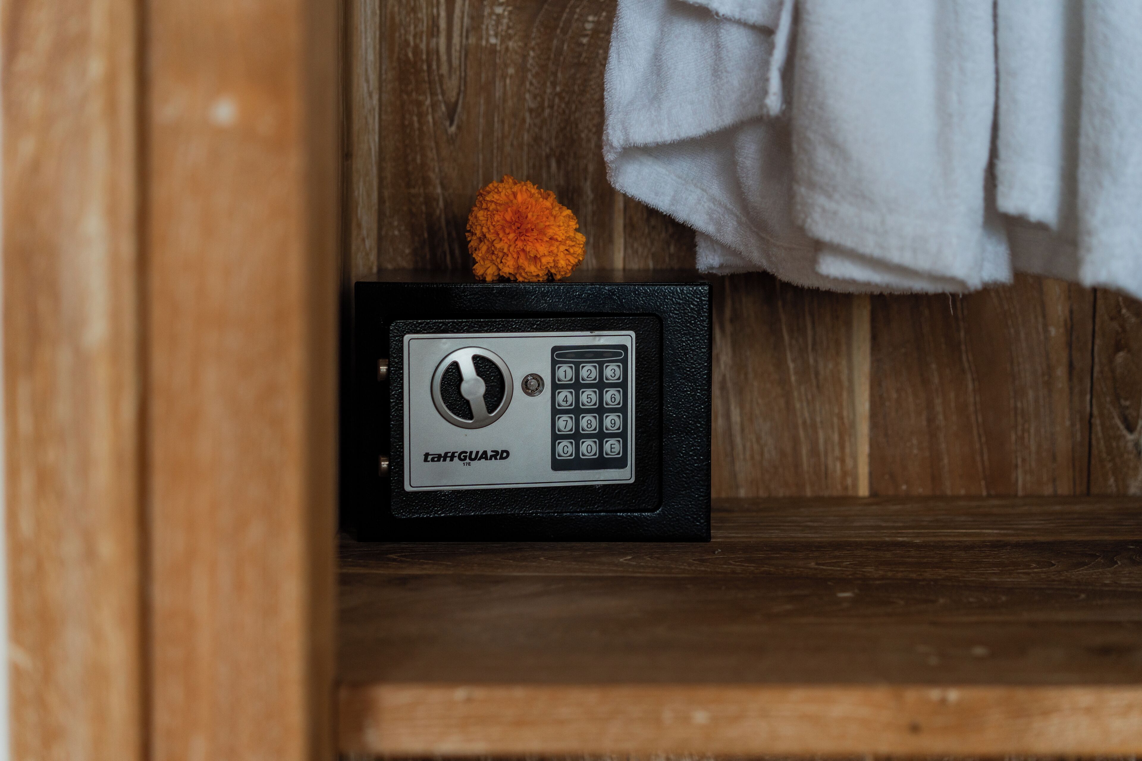 A black safe with a keypad and a flower on top, placed on a wooden shelf.