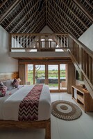 A spacious bedroom with a large bed, a wooden staircase, and a balcony with a view of the outdoors.