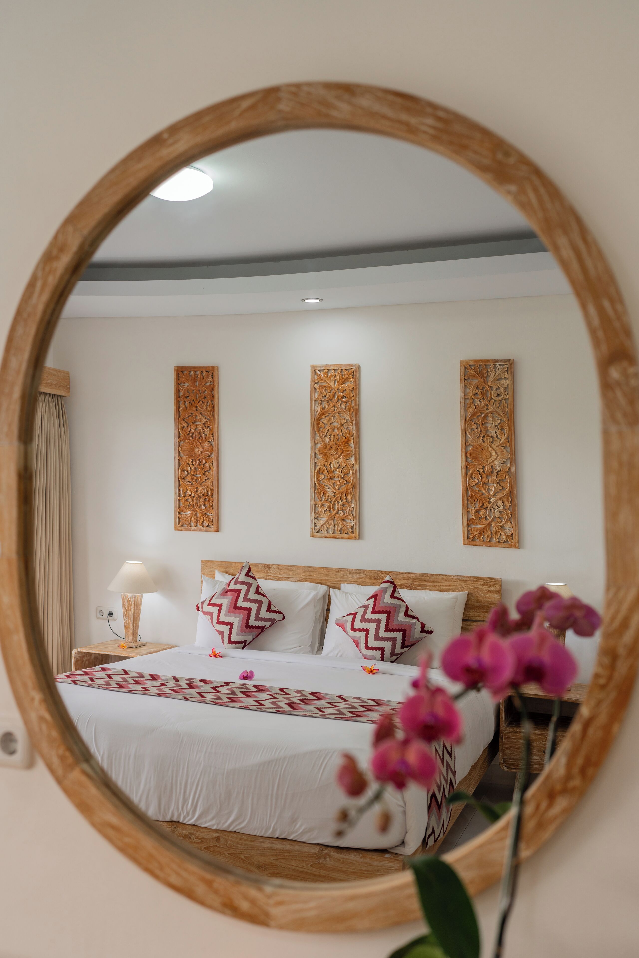 Un dormitorio con cabecera de madera, una cama con almohadas estampadas, una mesita de noche con lámpara y paneles decorativos en la pared.
