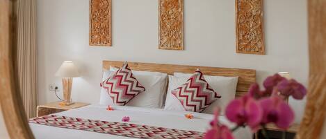 Un dormitorio con cabecera de madera, una cama con almohadas estampadas, una mesita de noche con lámpara y paneles decorativos en la pared.