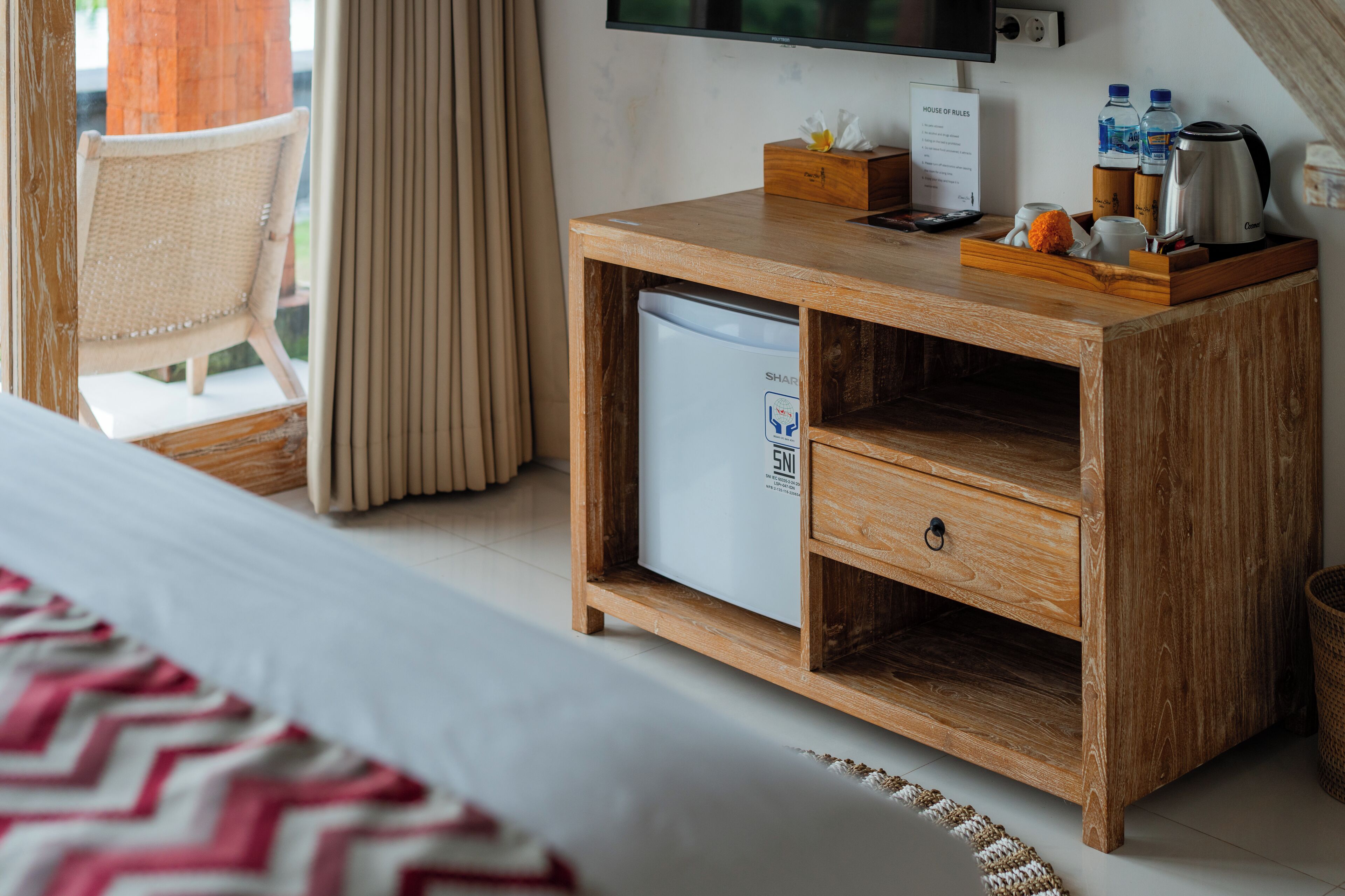 Ein Hotelzimmer mit einem Holztisch, einer kleinen Kühlbox, einem Fernseher und einem Bett mit gemustertem Überwurf.