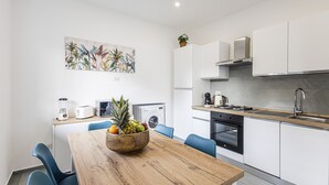 Une cuisine moderne avec des meubles blancs, une table à manger en bois et un panier de fruits.