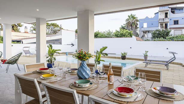 Un espace repas avec vue sur la piscine, une table en bois, des chaises et un vase rempli de fleurs.