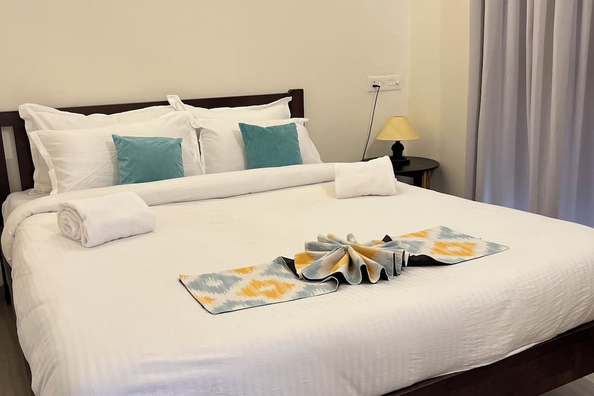 A neatly made bed with white linens, teal pillows, and a decorative towel arrangement.