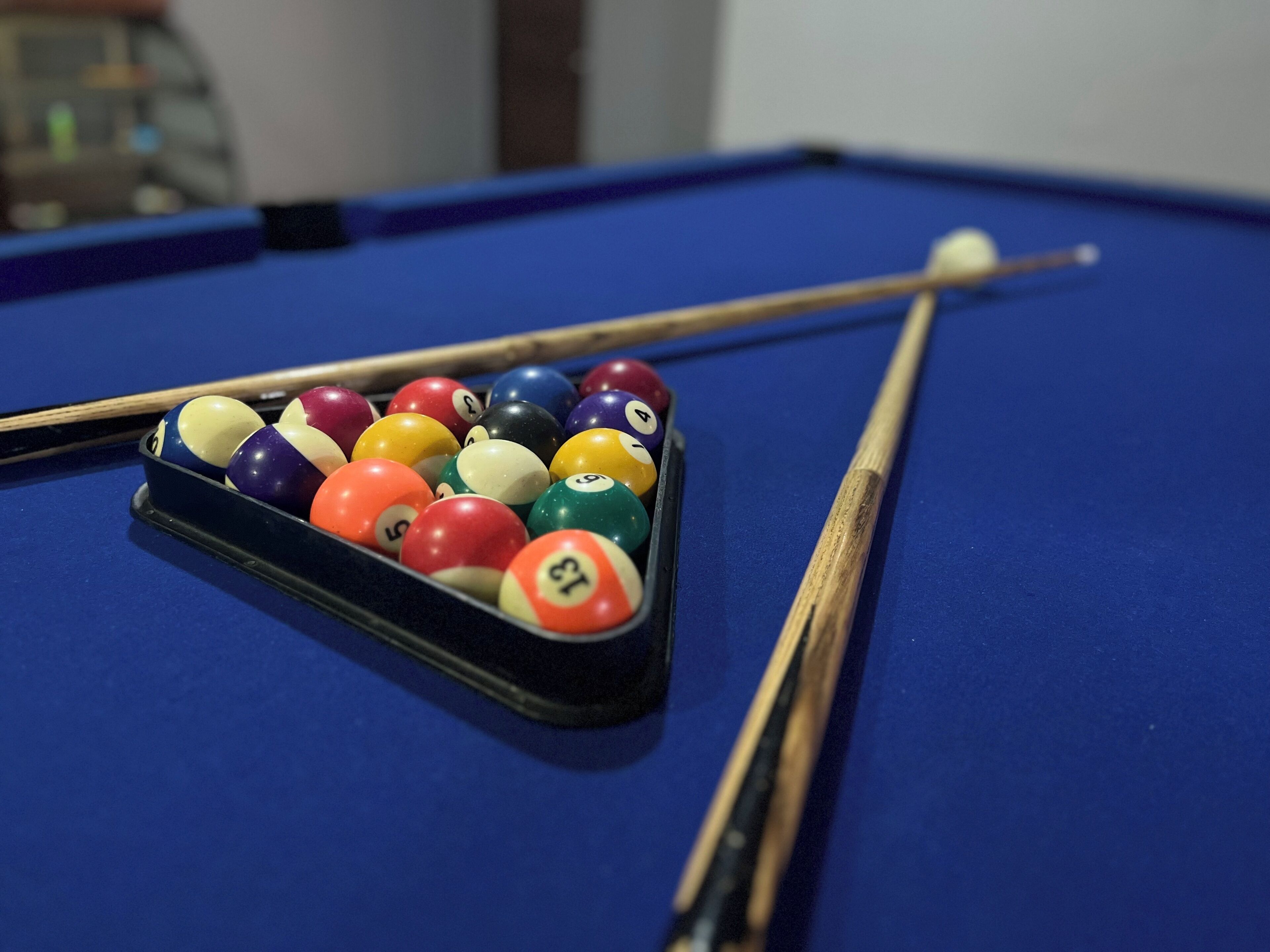 A pool table with a rack of billiard balls and a cue stick.