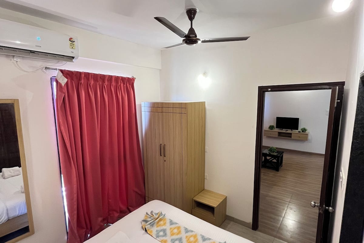 A hotel room with a bed, a wardrobe, a ceiling fan, and a television in the adjacent room.