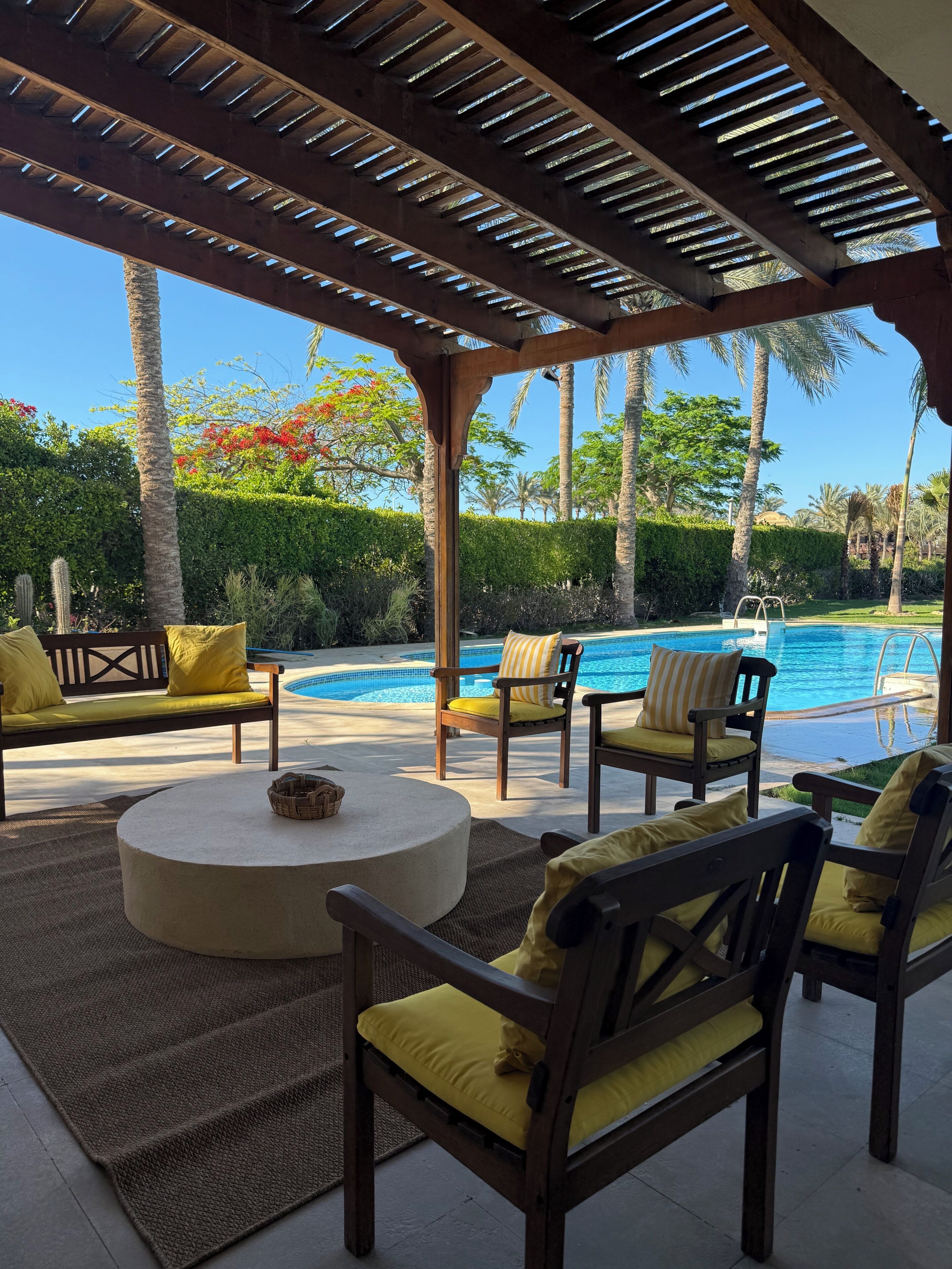 Un espace extérieur aménagé avec des sièges, une piscine, une pergola en bois et des plantes tropicales.