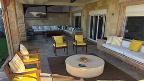 Ein Terrassenbereich im Freien mit einer Steinsäule, einer Polstergarnitur aus Holz und einem runden Couchtisch.