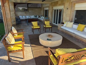 An outdoor patio area with a stone wall, a wooden sofa set, and a round coffee table.