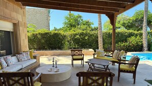 An outdoor patio with a sofa, chairs, a table, and a pool.