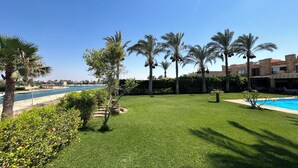 A well-maintained lawn with a pool, palm trees, and a view of the sea.
