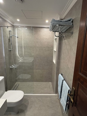 Une salle de bain avec une douche Ă parois de verre, des toilettes et un porte-serviettes avec des serviettes.