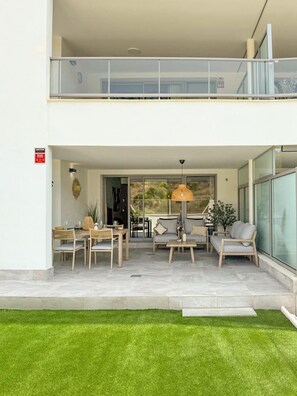 Una casa moderna de dos pisos con balcón, un área de comedor con mobiliario exterior y un césped bien cuidado.