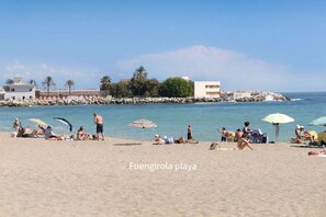 Ein Strand mit Menschen, Sonnenschirmen und einem Gebäude im Hintergrund.