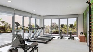 A modern gym with treadmills, exercise bikes, and free weights. Large windows offer views of greenery outside. - Célere Vitta Nature - Mijas costa, Andalucía (Mijas costa)