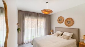 A bedroom with a large bed, a hanging light fixture, a mirror, and a window with curtains. - Célere Vitta Nature - Mijas costa, Andalucía (Mijas costa)