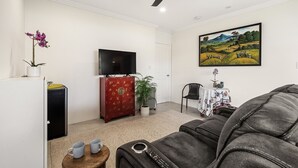 A living room with a flat-screen TV, a red cabinet, a ceiling fan, a painting, and a sofa.