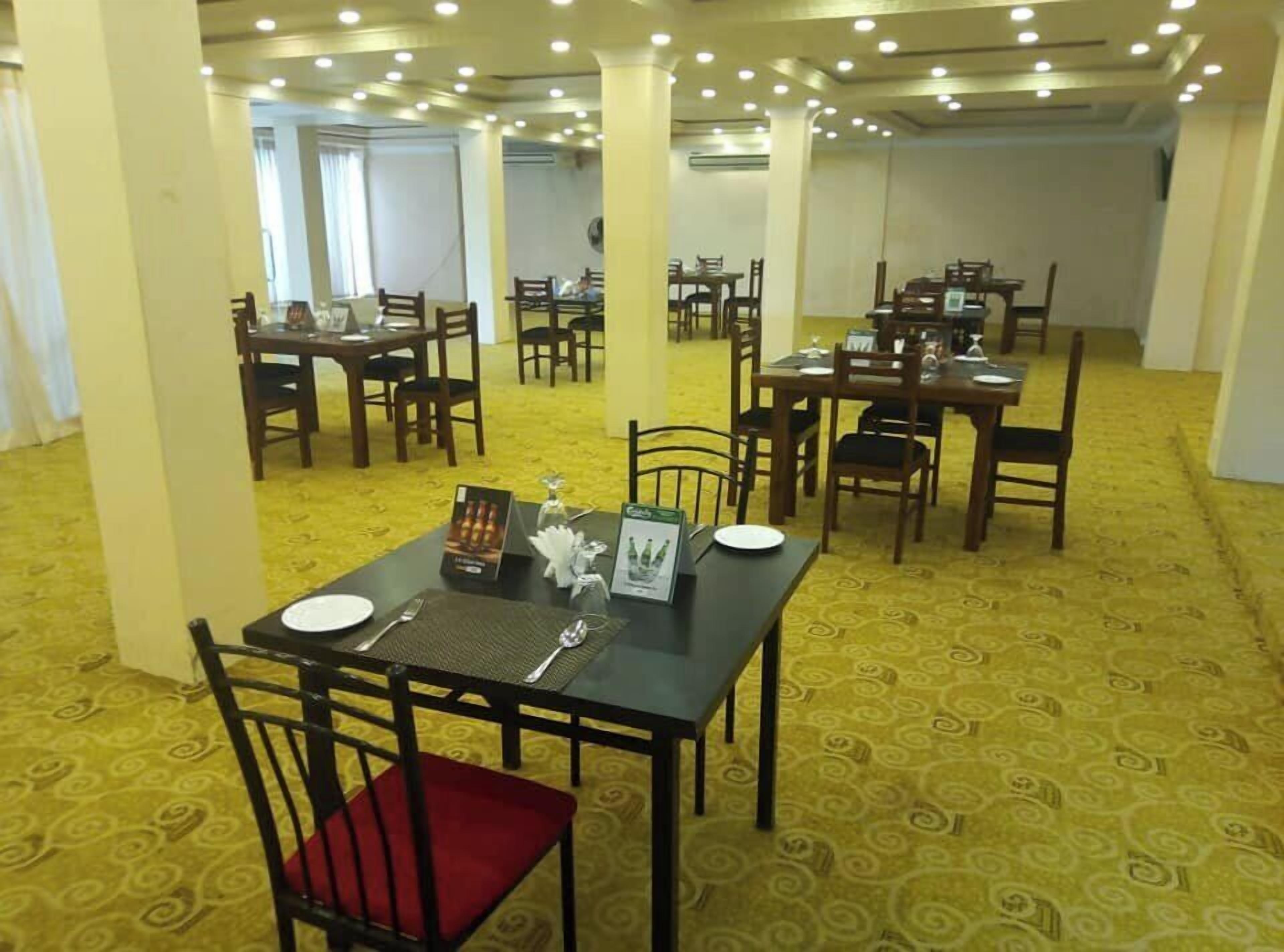A dining area with multiple tables and chairs, carpeted floor, and ceiling lights.