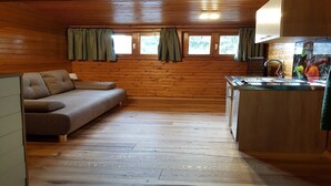 A cozy cabin interior with a sofa, wooden walls, a kitchen area, and windows with curtains. - Apartment near Romerbad Thermal Spa (Bad Kleinkirchheim)