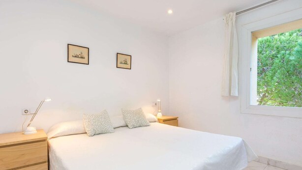A bedroom with a large bed, two bedside tables, two wall-mounted picture frames, a window with a view of greenery, and a white curtain. - Apartment near Romerbad Thermal Spa (Bad Kleinkirchheim)