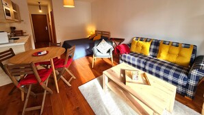 A cozy living room with a plaid sofa, a wooden coffee table, a dining table with chairs, and a small kitchen area. - Bad Gastein Fallside Apartment (Bad Kleinkirchheim)