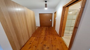 A narrow hallway with wooden flooring and walls, leading to a door and a glass shower area. - Bad Gastein Fallside Apartment (Bad Kleinkirchheim)