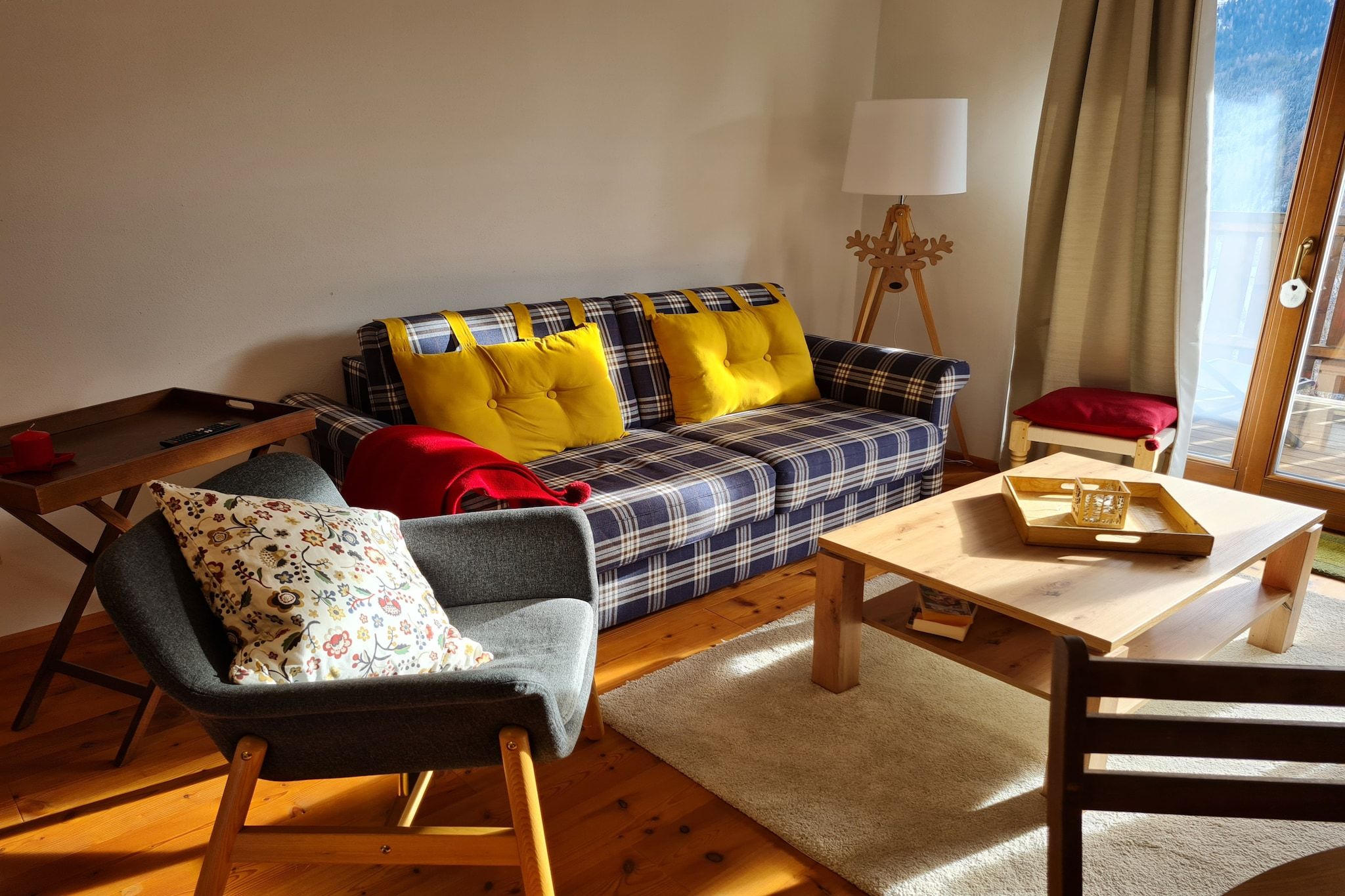 Un salon chaleureux avec un canapé à carreaux, une table basse en bois, un fauteuil gris et une lampe.