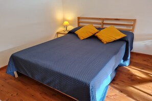 A bed with a blue quilted cover, two mustard-colored pillows, and a wooden headboard.