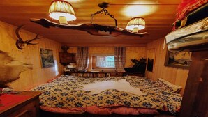 A cozy room with a bed, wooden walls, a chandelier, and a window with curtains.