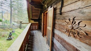 A wooden cabin with a balcony, a wooden wall with a sun design, and a fenced yard with a statue.