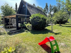 Eine rustikale Holzhütte mit einem strohgedeckten Dach, einer Veranda und einer kleinen Terrasse.