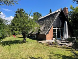 A traditional house with a thatched roof, a brick chimney, and a white door.