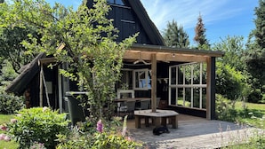 Una terraza de madera con una mesa y sillas, rodeada por un jardín con diversas plantas y flores.
