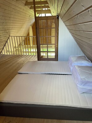 Ein Schlafzimmer mit Holzbalkendecke, einer Matratze und Blick durch eine Tür.