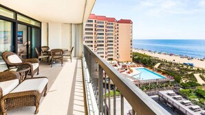 A balcony with wicker furniture, a pool, and a view of the beach and ocean.