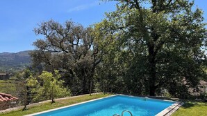A rectangular swimming pool with a metal ladder, surrounded by grass and trees, with a mountainous landscape in the background. - Casa da Oliveira Pool Spa Wellness Retreat @Gerês (São Jorge)