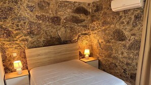 A bedroom with a stone wall, a wooden headboard, a bed with white bedding, two bedside lamps, and an air conditioning unit. - Casa da Oliveira Pool Spa Wellness Retreat @Gerês (São Jorge)