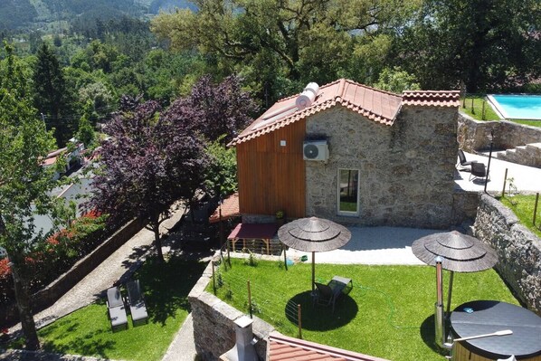 A stone building with a tiled roof, surrounded by a well-maintained lawn and outdoor seating area with umbrellas.
