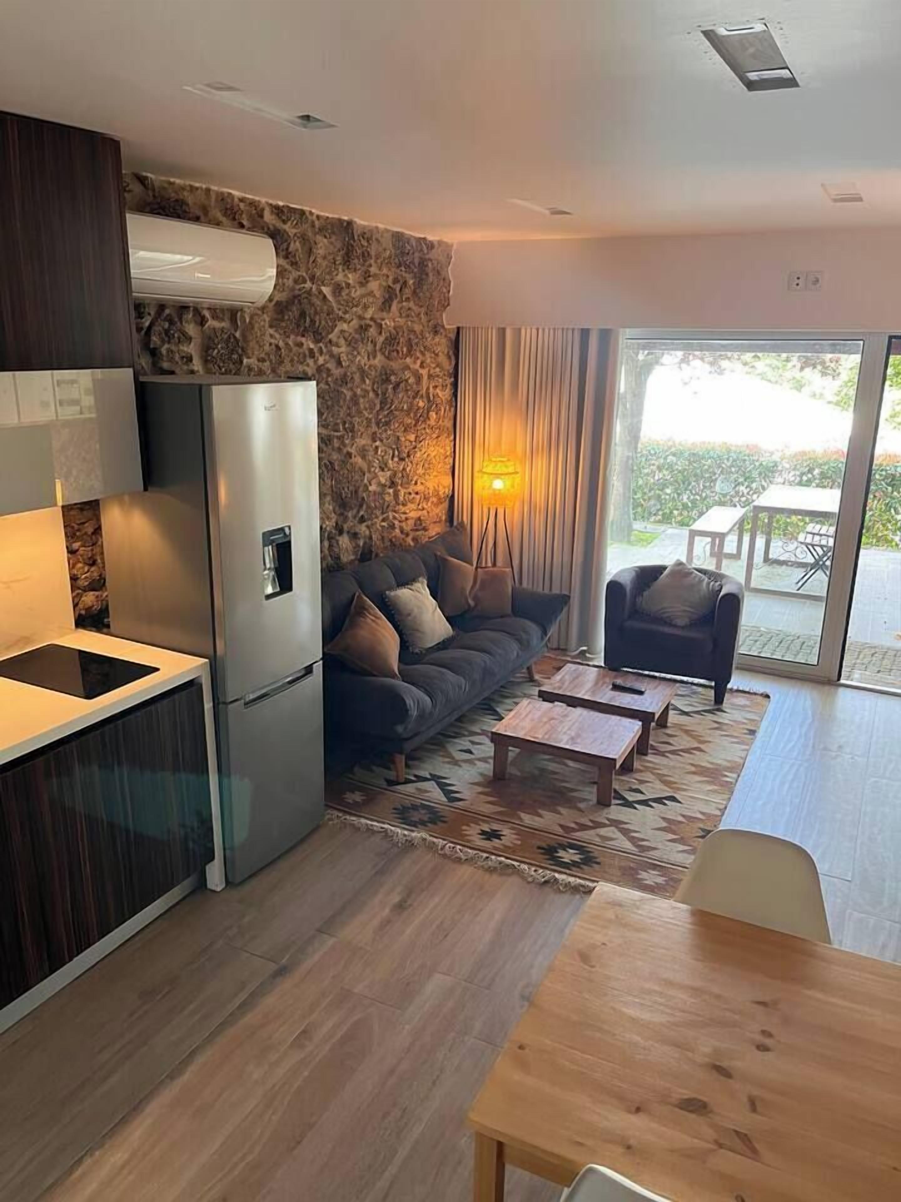 Un espacio de estar moderno con cocina, sofá, zona de comedor y vistas a través de un ventanal.