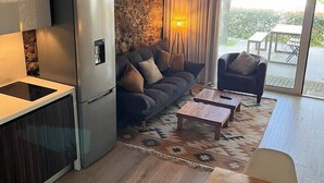 A modern living space with a kitchen, a sofa, a dining area, and a view through a glass door. - Casa da Oliveira Pool Spa Wellness Retreat @Gerês (São Jorge)