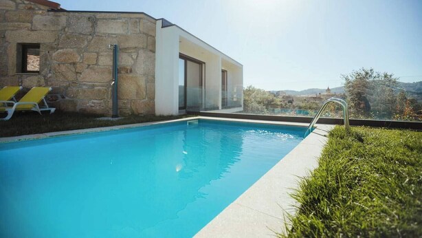 A modern pool area with a stone building, a glass door, and a clear view of the landscape.