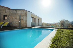 A modern pool area with a stone building, a glass door, and a clear view of the landscape.