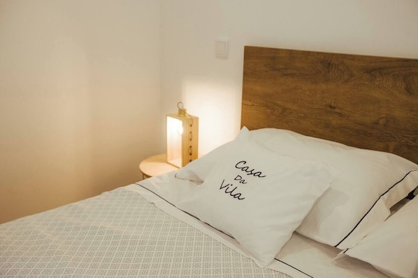 Una cama bien hecha con una colcha estampada, cabecera de madera y un cojín con texto.