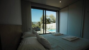 A bedroom with a bed, a window with a view of a swimming pool and greenery, and a towel on the bed.