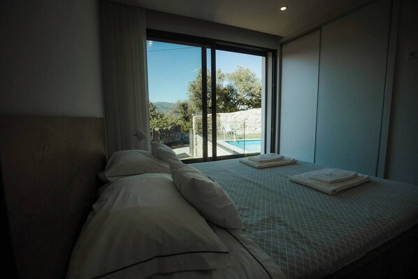 Un dormitorio con una cama, una ventana que ofrece vistas a una piscina y vegetación, y una toalla sobre la cama.