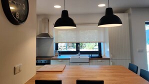 A modern kitchen with a wooden dining table, pendant lights, and a view of the outdoors.