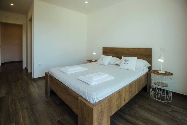 A neatly made bed with white linens and pillows, a wooden headboard, and a bedside table with a lamp.