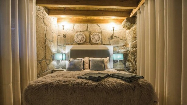 A cozy bedroom with a stone wall, a fluffy bed, and two bedside lamps.