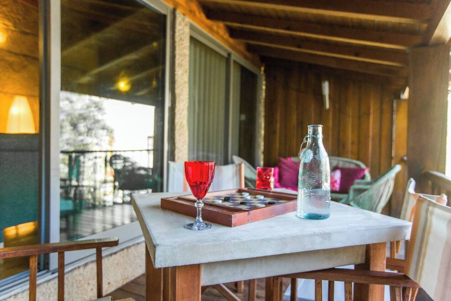 Una terraza de madera con una mesa preparada para dos personas, que incluye un vaso y una botella.